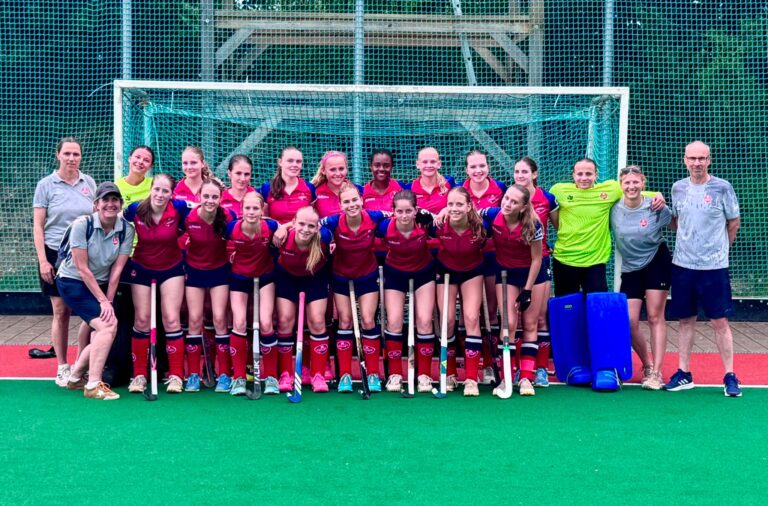 Hockey-Mannschaft mit Betreuerteam vor dem Tor auf dem Kunstrasenplatz